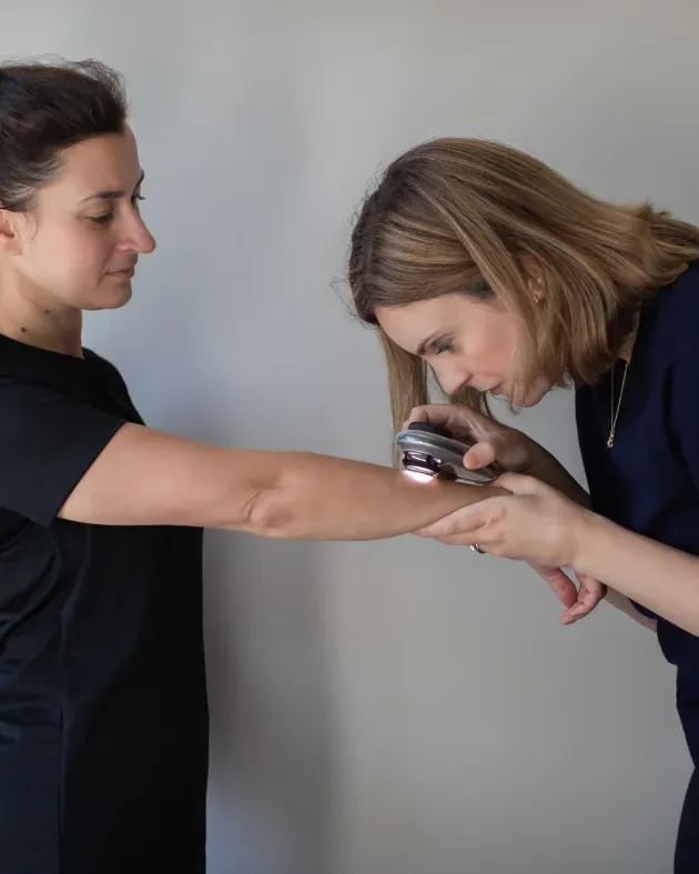 Dr Ella Seccombe examining a patient’s arm with a dermatoscope