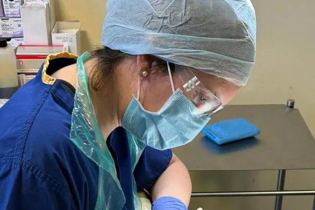 A surgeon in scrubs, mask and safety glasses performing skin surgery